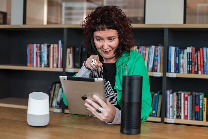 A woman talking to an ipad points at the device, as though accusing it of something.