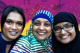 Three woman in front of a colourful pink and yellow background for a story about cooking in isolation during Ramadan.
