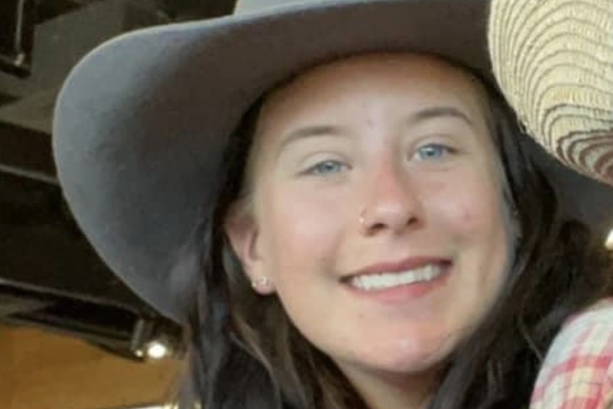 A smiling young woman with a nose piercing, wearing a broad-brimmed hat.