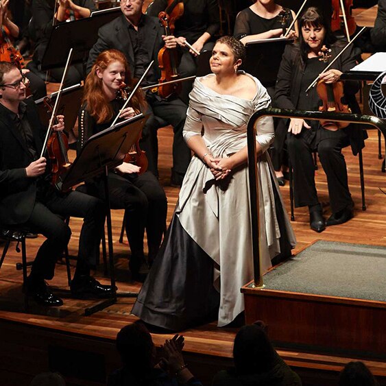 Soprano Deborah Cheetham standing at the front of the Melbourne Symphony Orchestra on the stage at Hamer Hall