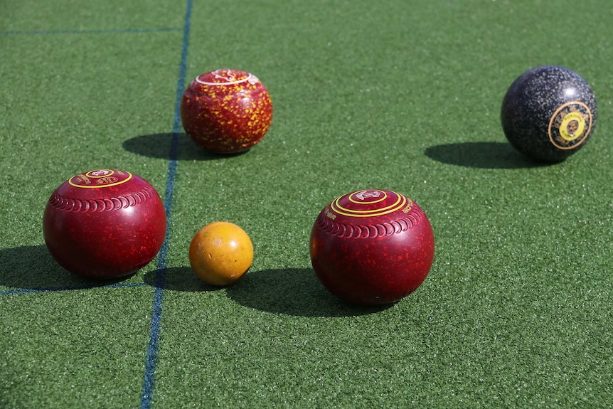 Red and black lawn bowls next to a yellow jack.