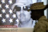 A US Marine walks past a television showing a portrait of US soldier Specialist Jeremy Sivits.