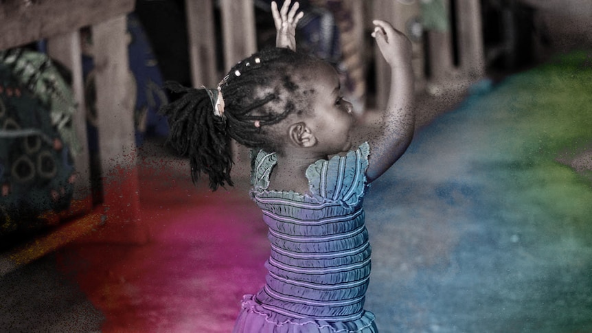 A photograph of a small child in a blue dress waving her arms above her head while dancing.