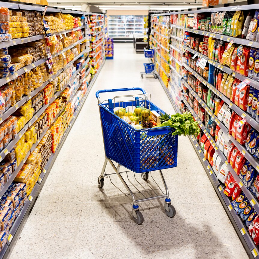 A shopping trolley of food is parked in the middle aisle of the supermarket surrounded by colourful packaging 