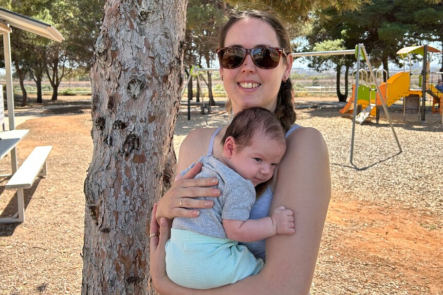 A woman holding her newborn son at a park.