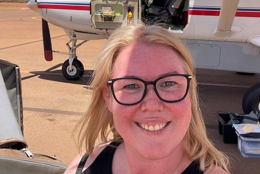 A British teacher smiling in front of a light airplane on the runway at Newman airport in Western Australia's Pilbara region.