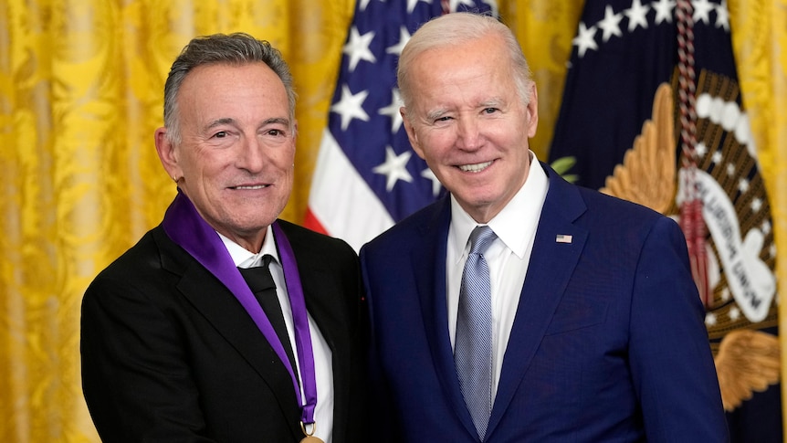 Bruce Springsteen, with a medal around his neck, stands next to Joe Biden