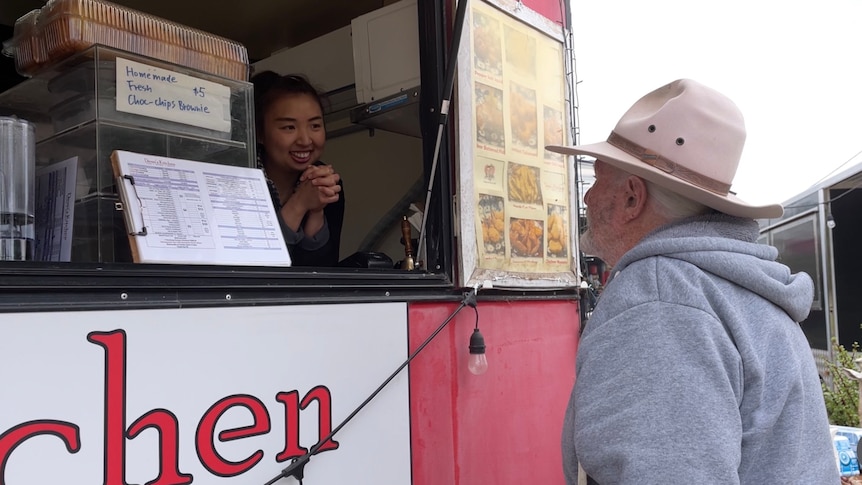 Taiwanese-Australian woman Demi Tsai smiles at a grey-haired customer in an akubra from her red food van.