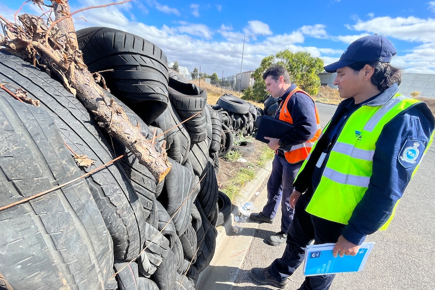 Man in high-vis standing next to a pile of dumped tyres.