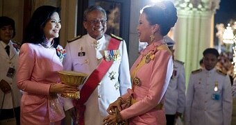 Princess Ubolratana stands and smiles in pink outfit with light shining behind her.