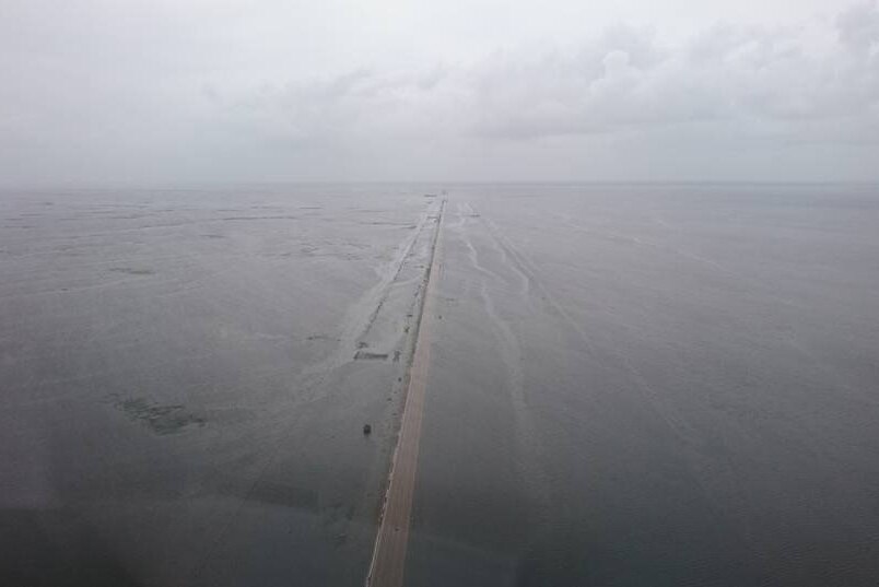 Birds eye view of a long straight road and landscape completely flooded.
