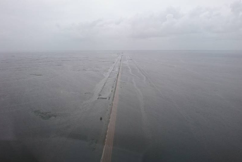 Birds eye view of a long straight road and landscape completely flooded.