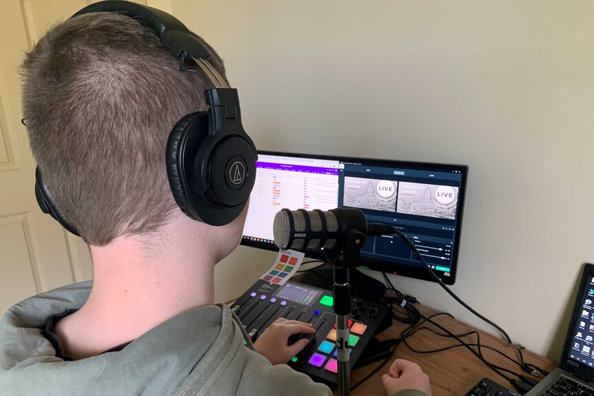 A teenage boy wearing headphones looks at a computer screen and speaks into a microphone.