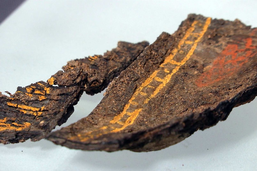 A brown segment of wood with yellow and orange lines in paint.