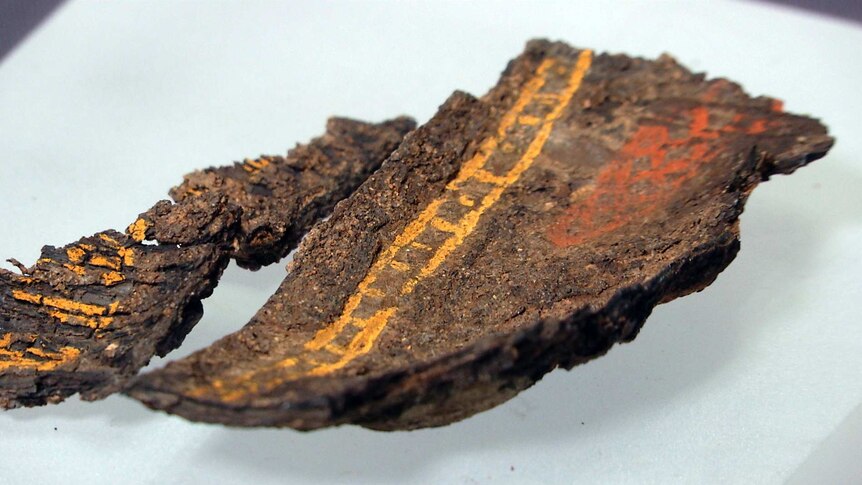 A brown segment of wood with yellow and orange lines in paint.