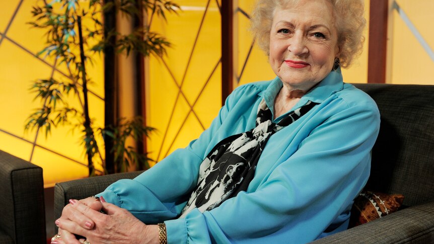 Betty White sits on an armchair smiling 