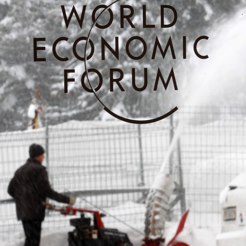 A worker removes snow in front of a logo from the World Economic Forum in Davos, Switzerland.