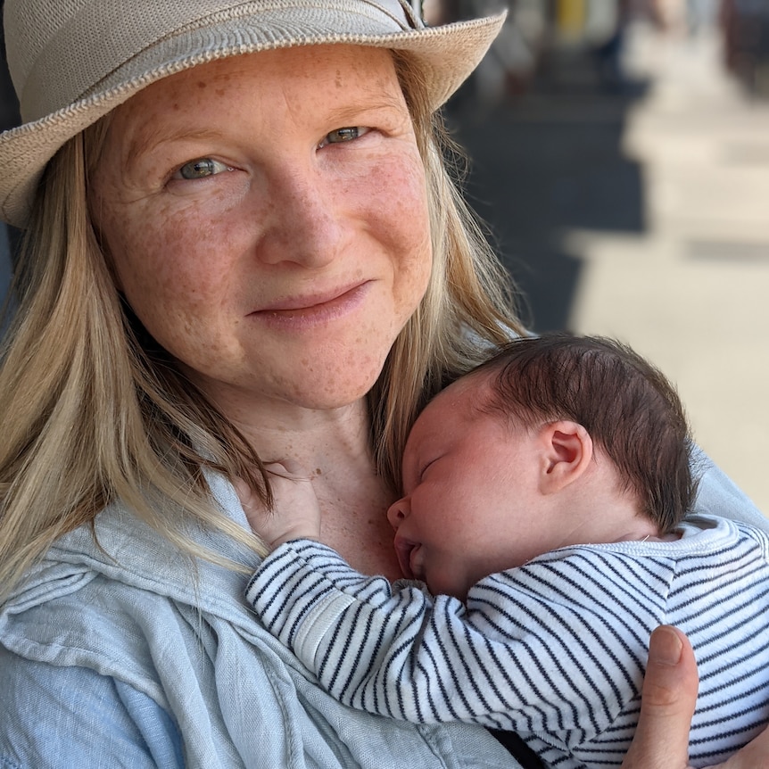 A smiling woman wearing a straw hat holds a young baby to her chest.