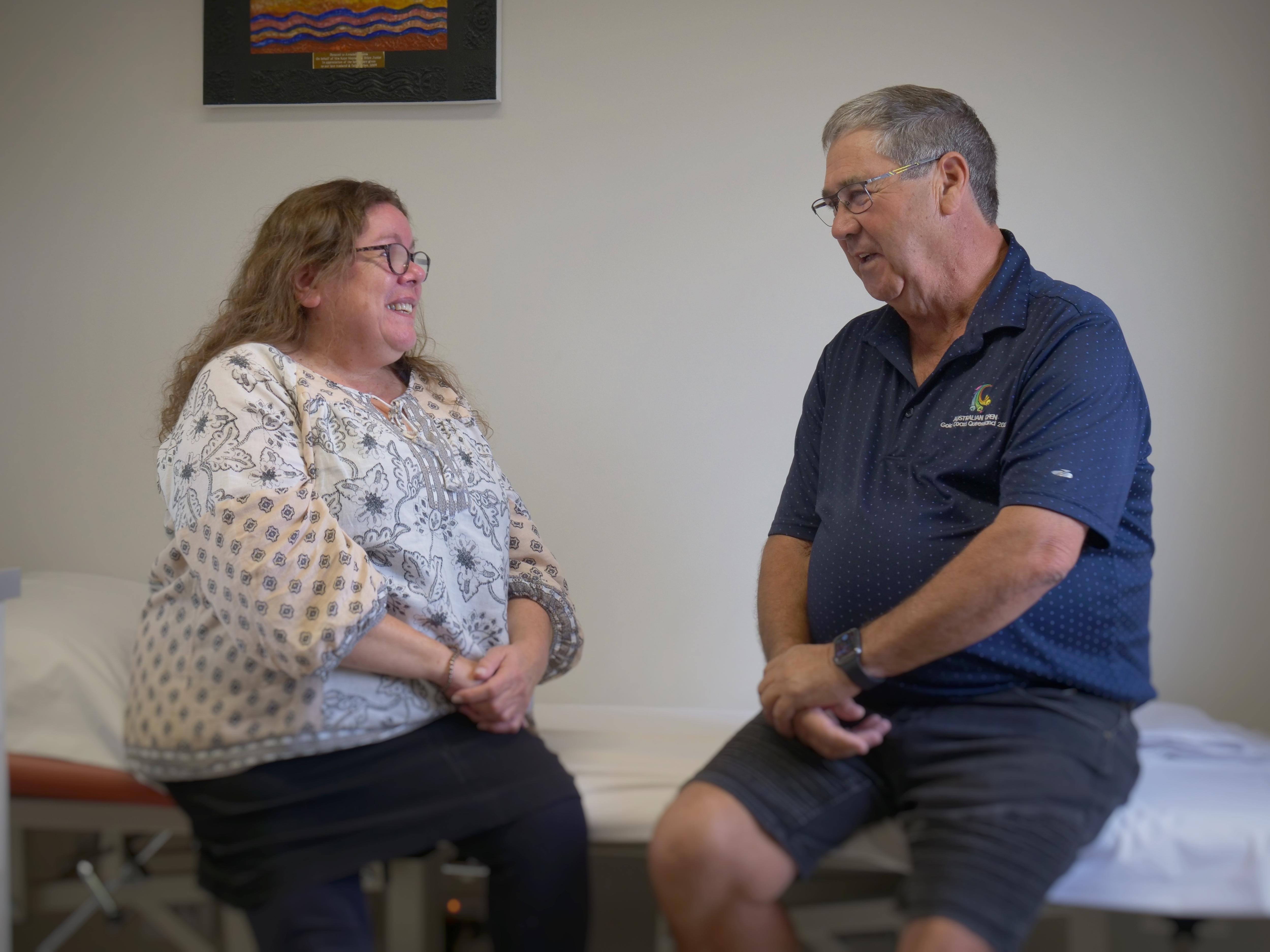 A woman and man sitting on a doctor's bed have a chat