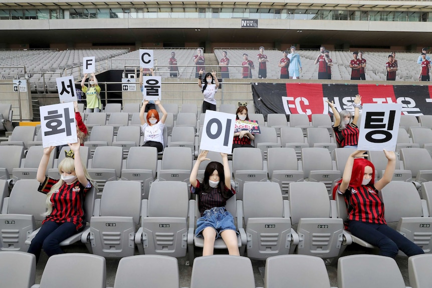 Female sex dolls are posed in a stadium wearing a soccer team's uniform and cut outs of players are lined up.