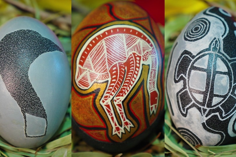 Three carved and painted emu eggs, depicting emus and a turtle. They are grey, deep purple, black and red.