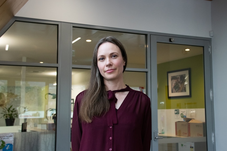 Young woman stands in front of glass windows in office.