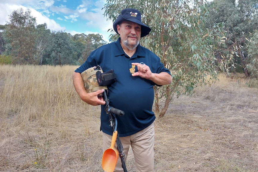 a man holds a metal detector and a piece of gold