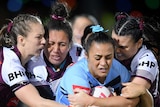 A rugby league player stands crouched over while being tackled by three opponents in the Women's State of Origin match.