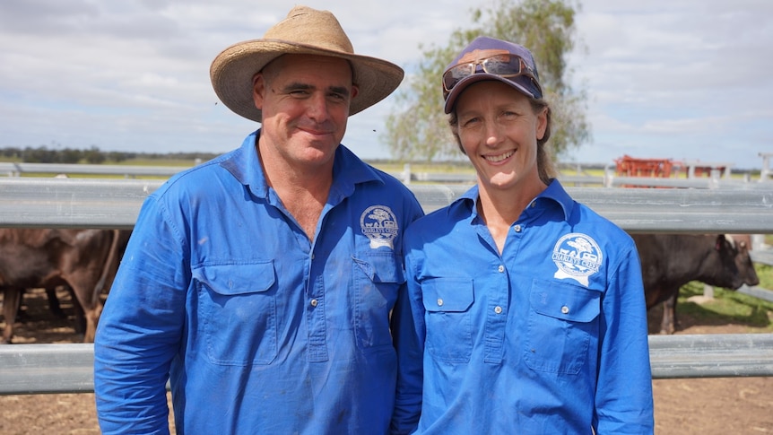 A smiling man and a woman, both wearing hats and work gear, on a cattle farm.