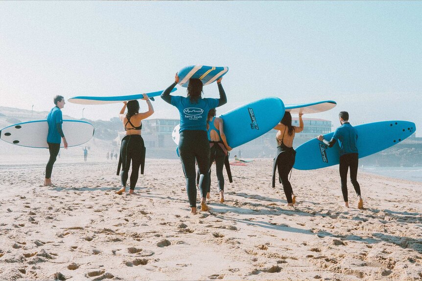 A group of young people on a beach with surf boards to depict how to deal with feeling lonely and isolated.