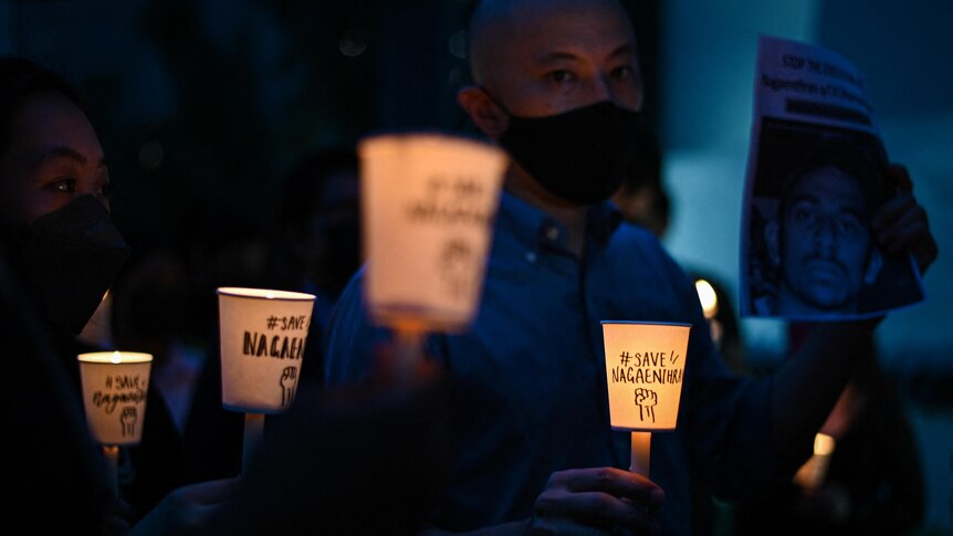 Blue shadows surrounds several people holding cups lit by candles. 