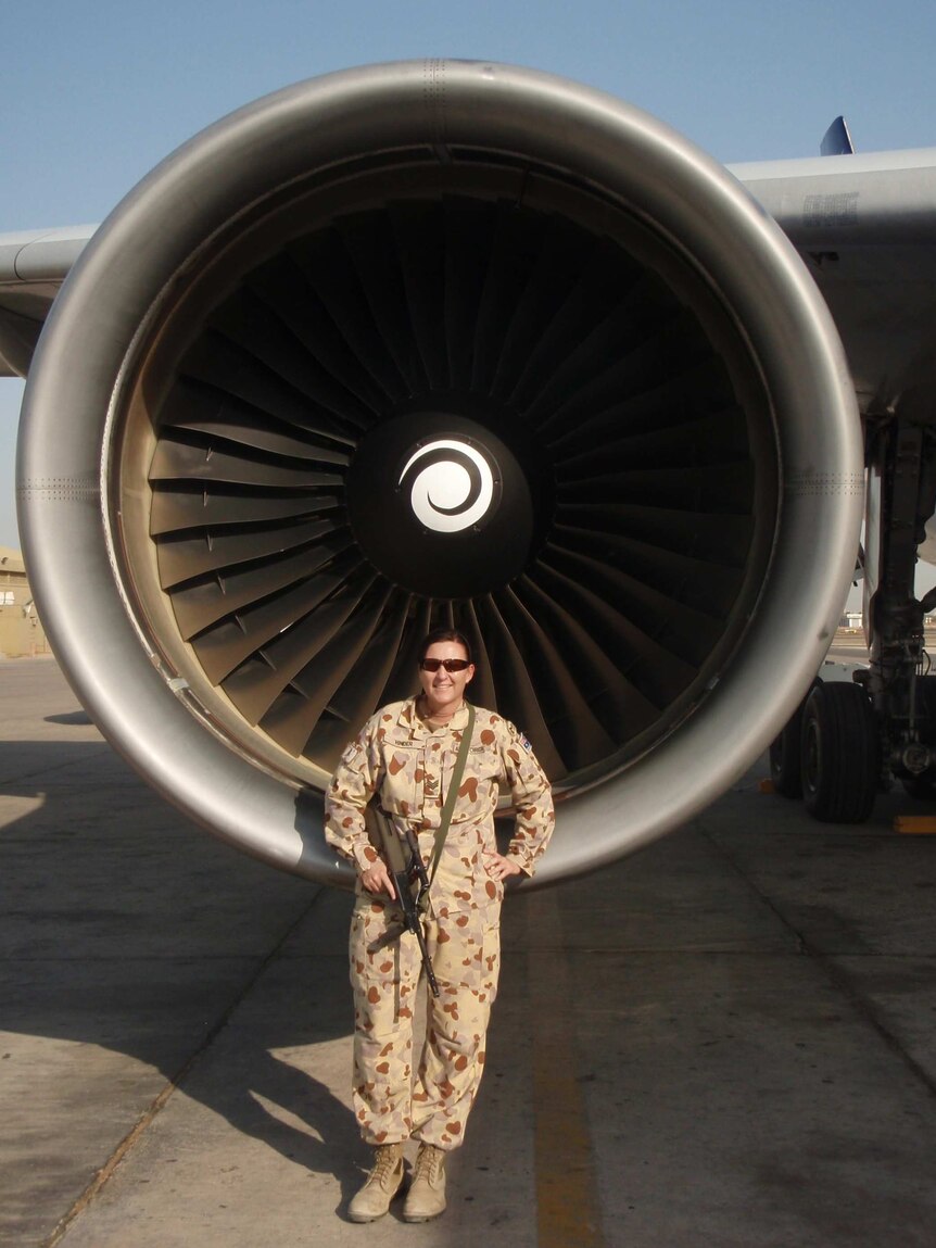 Army and Air Force veteran Karyn Hinder stands in uniform in front of the jet turbine of a large plane.