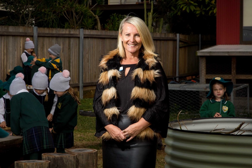 Kim Moroney stands in the middle of a playground with kids next to her.