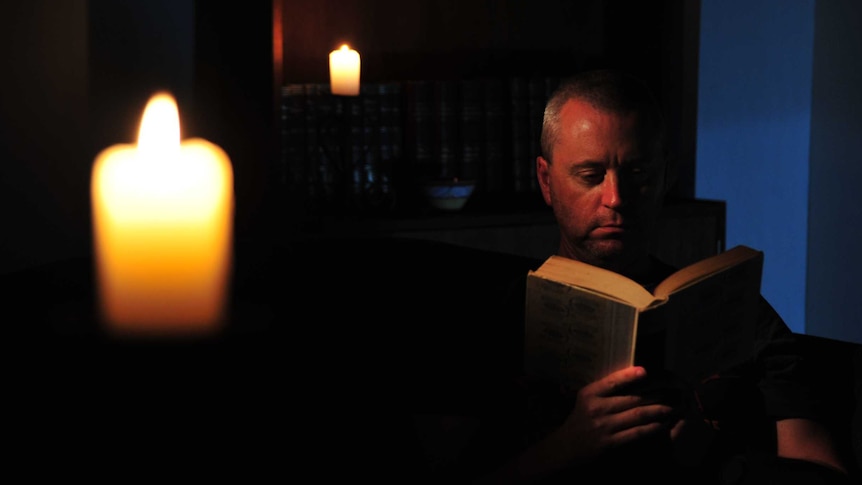 A man reads by candlelight during a blackout.