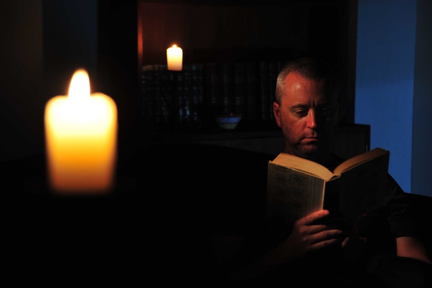 A man reads by candlelight during a blackout.