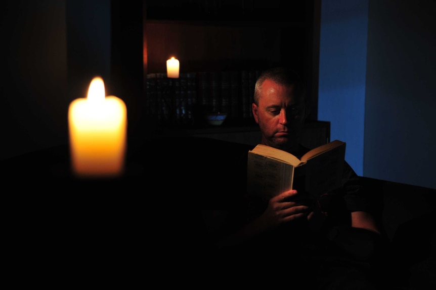 A man reads by candlelight during a blackout.