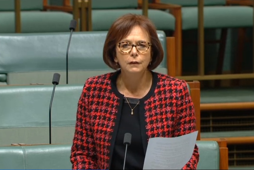 woman in parliament holds paper with short brown hair and red and black jacket. 
