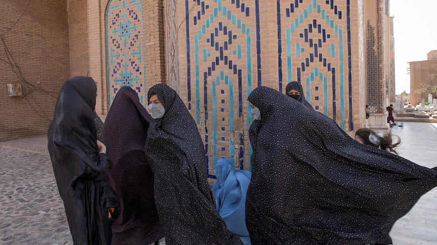 Women in long hijab walk near a mosque. 