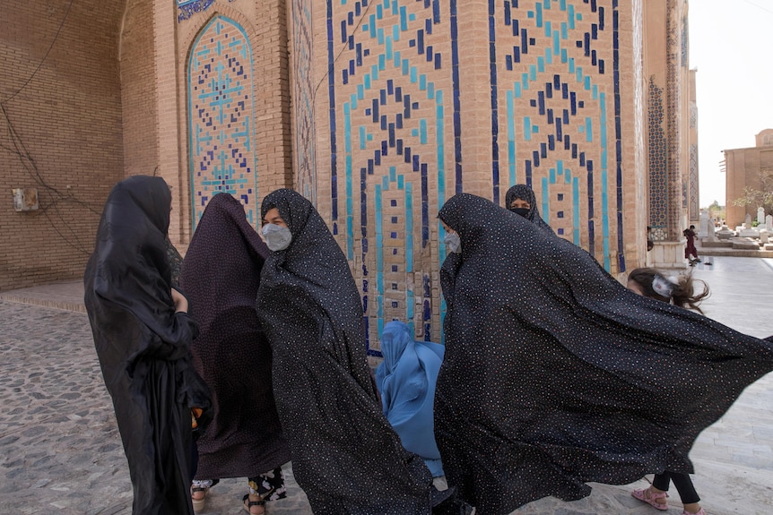 Women in long hijab walk near a mosque. 