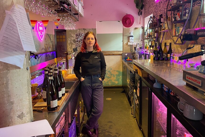 A woman stands with her hands in her pocket behind a bar.