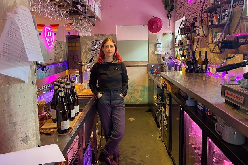 A woman stands with her hands in her pocket behind a bar.