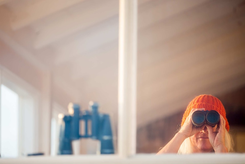 Karen Bragg, wearing an orange beanie, looks through a pair of binoculars.