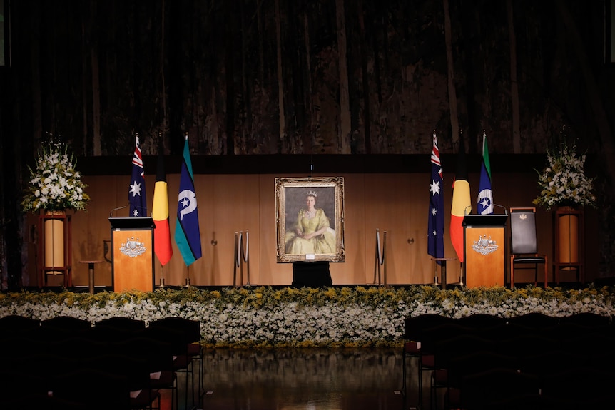 A portrait of the Queen sits in the middle of two podiums with the Australian, Aboriginal and Torres Strait Island flags behind