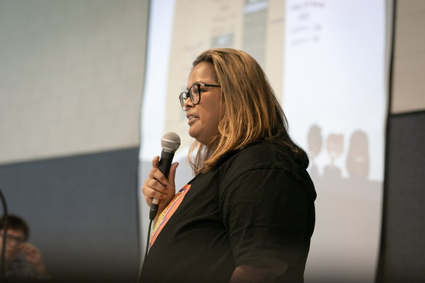 A woman with glasses holds a Mic and addresses a meeting in Katherine. 