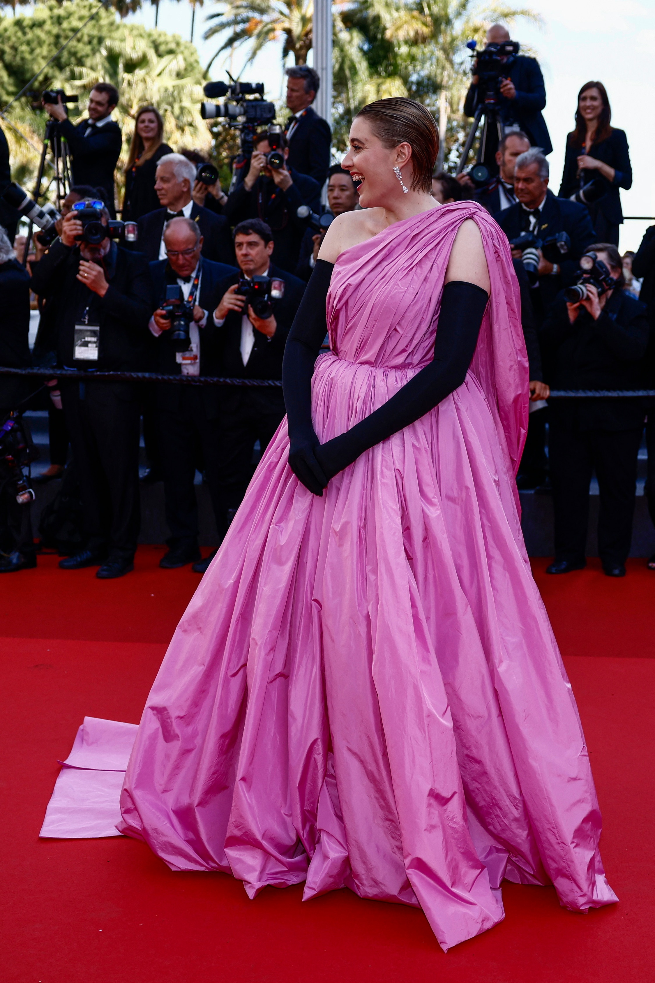 Greta Gerwig wearing a long puffy pink dress with a long sash over one shoulder