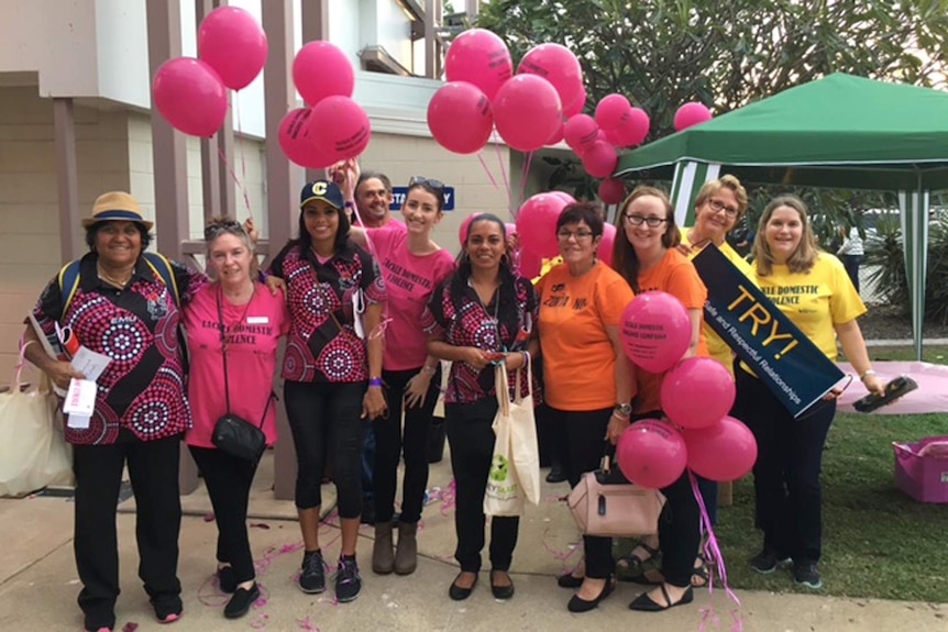 A group of people wearing bright t-shirts hold a banner reading 'tackle domestic violence'