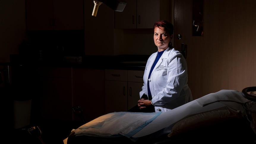 A doctor in a white coat sits in a surgical theatre.