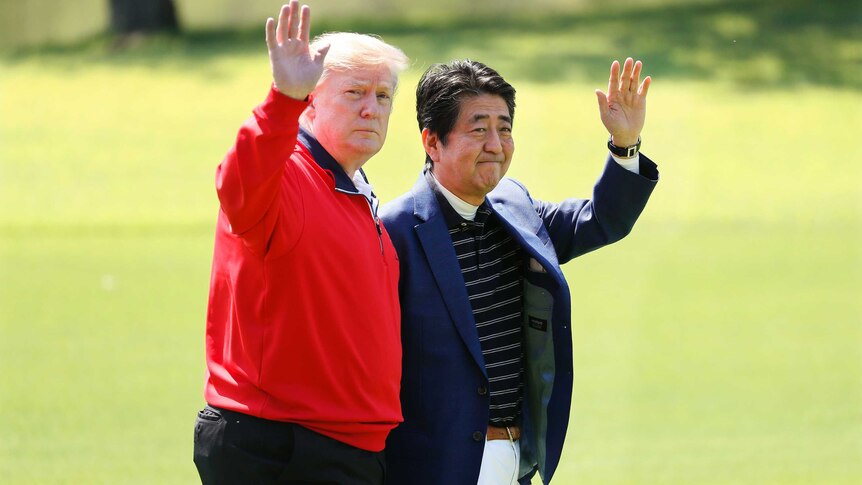 Mr Trump and Mr Abe wave to cameras as they walk on a golf course.