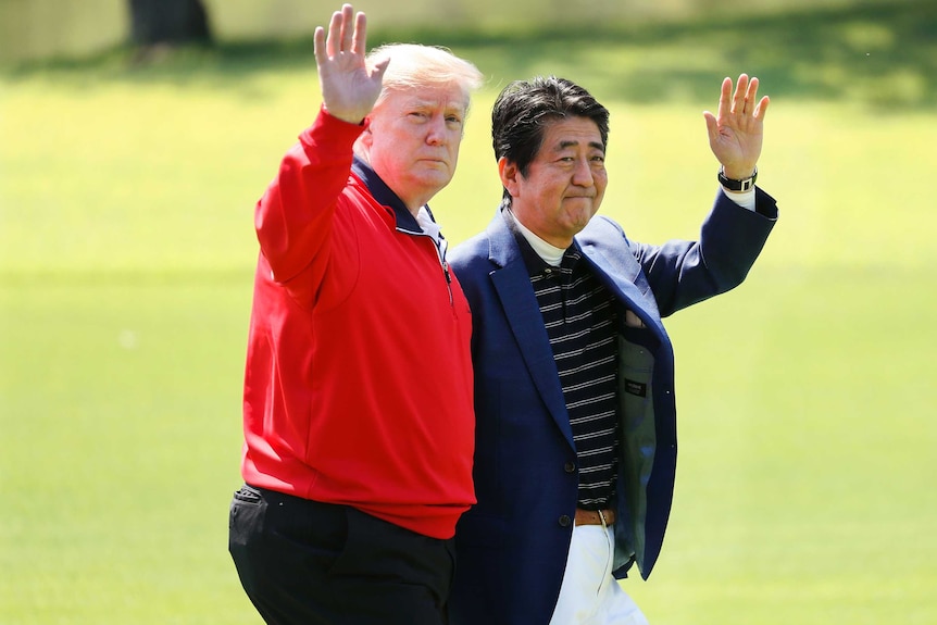 Mr Trump and Mr Abe wave to cameras as they walk on a golf course.