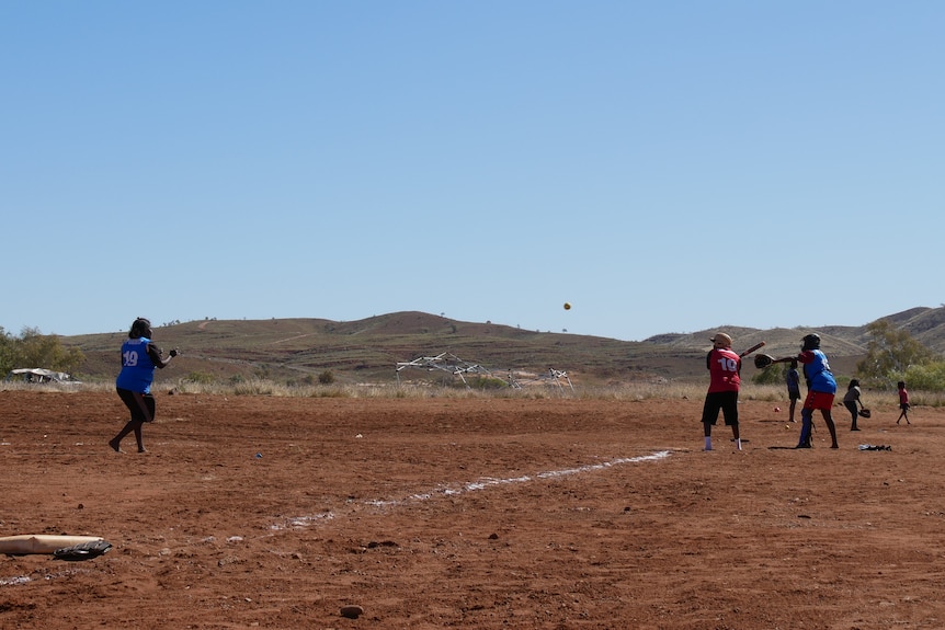 Women playing softball on a red dirt field.